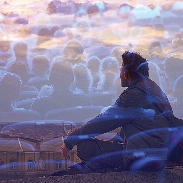 A man sitting and staring at a city skyline with faded faces in the background