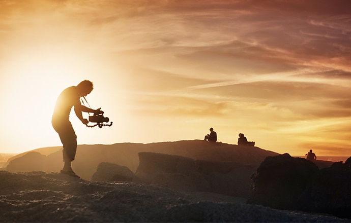 Man bending over a camcorder, filming in the desert