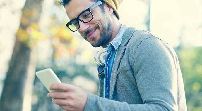 A young male with a beanie hat smiling into his mobile phone