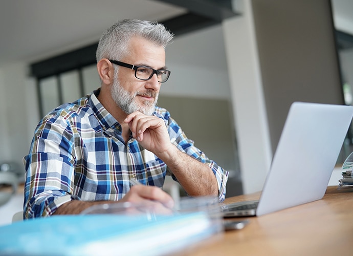 Man sitting at desk looking at laptop screen.