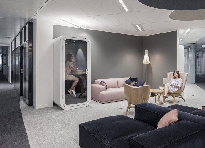 Image of another of Capgemini's breakout spaces within their office. A woman is sat in an armchair whilst another is in a private meeting booth.