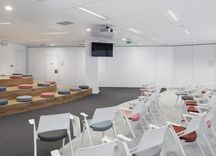 Image showing the interior of one of Capgemini's large auditorium-style spaces, decorated in a modern and minimalist style. A professional display and projector is visible mounted to the wall and ceiling.