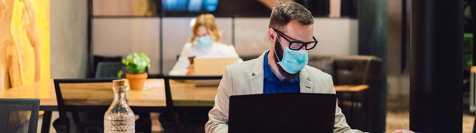 A man wearing a mask working in a socially distanced office with his laptop