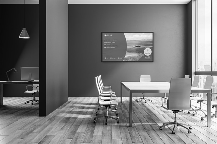 An empty office room with a BRAVIA professional display situated behind a table and chairs.