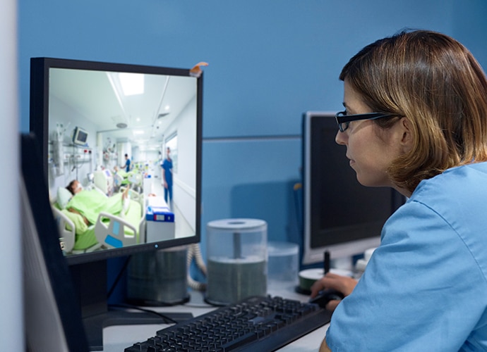 Woman wearing scrubs sitting at a desk looking at a monitor showing live video of a patient