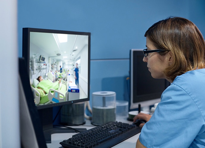 Nursing staff looking at ICU room on her monitor from an office