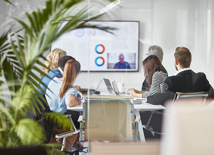 People working in a meeting room and hosting a call on the screen with a remote worker