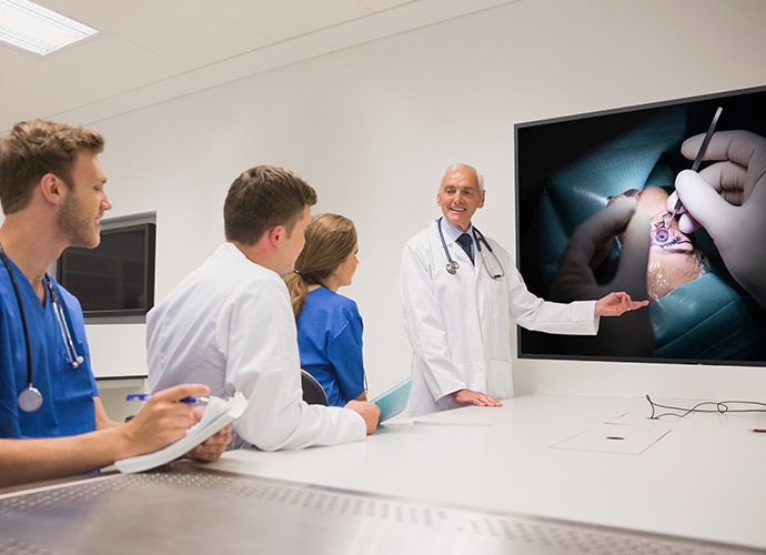 Doctor points at sony medical display with surgical image in a meeting room with fellow doctors