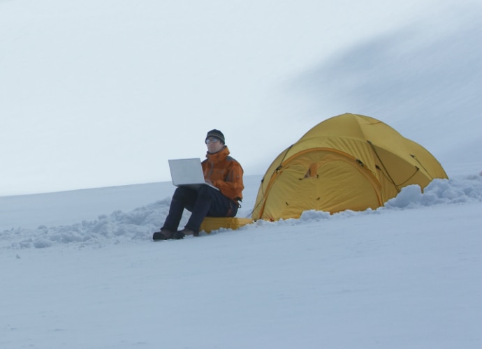 Man sitting remotely in the snow, looking at his laptop