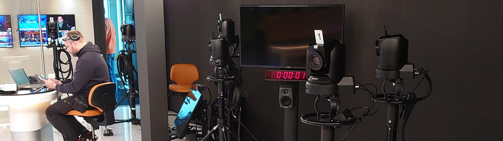 man sitting in front of laptop, and Bravia screens, looking at mobile device in a video production suite.