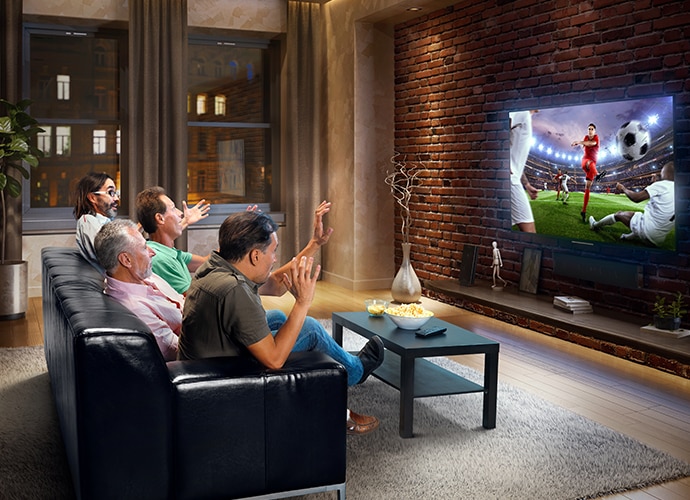 Four men sitting on a sofa facing a TV and watching football