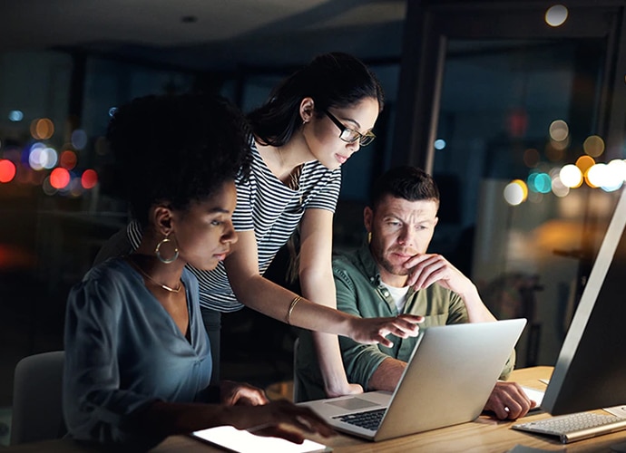 A man and two women looking at a laptop screen.