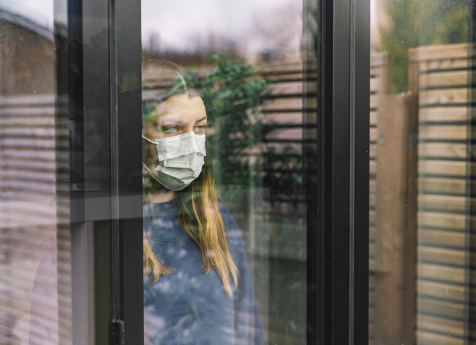 Ein Mädchen mit Maske, das aus dem Fenster schaut