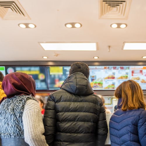 Customers in restaurant with menu board screens shown in the background