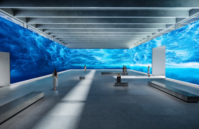 Image of exhibition with a video wall showing images of blue clouds