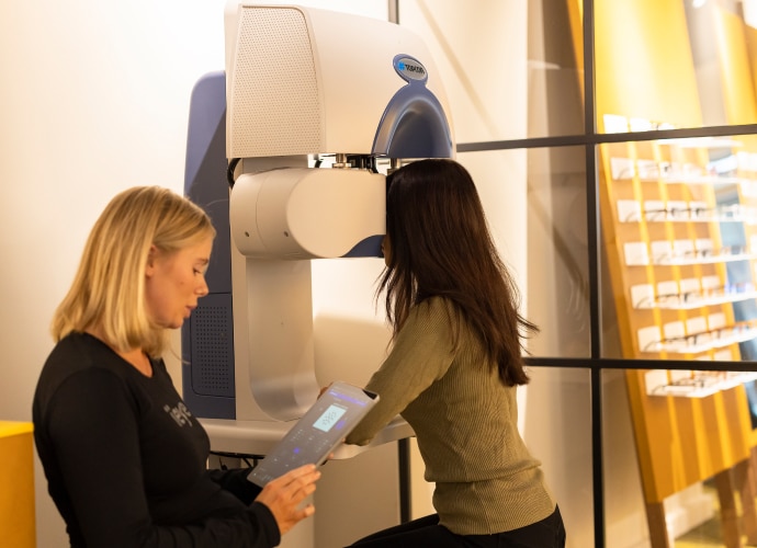 A woman using the eye testing machine and a woman next to her holding a tablet.