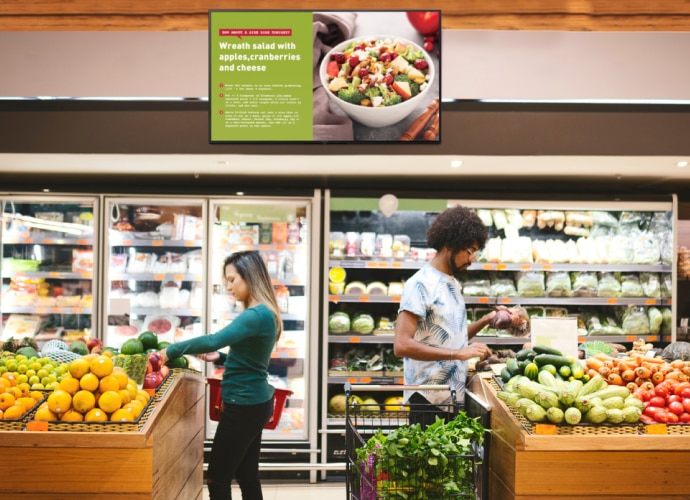 Two people in a supermarket with a display hung from the ceiling with recipes