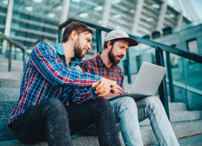 Two men are sitting on the stairs with a laptop