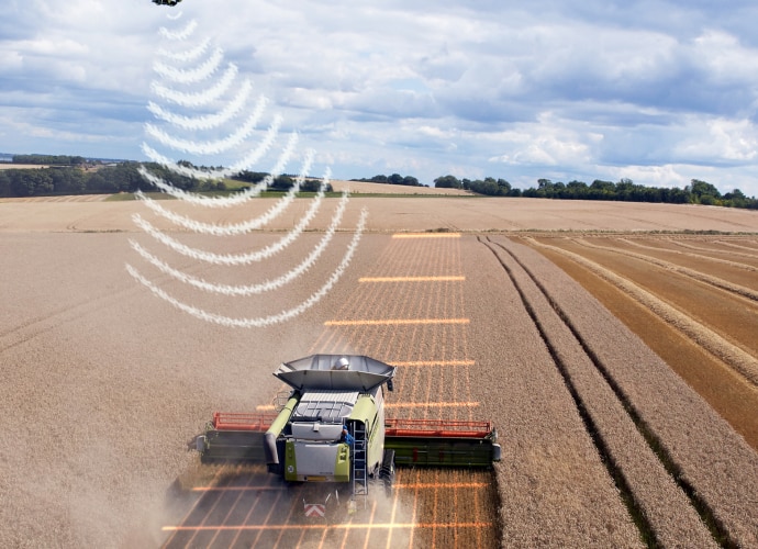 An agriculture machine driving through a field with drone in the air