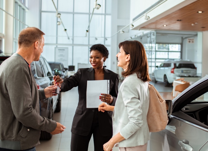 A woman handing car keys to a man and a woman