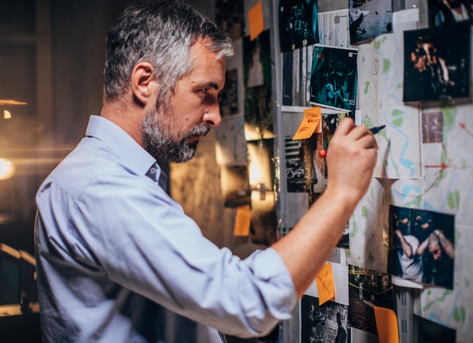 A detective is drawing on the map attached to the wall with crime images.