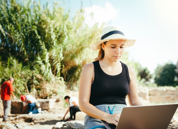 A woman at an archaeological site working on a laptop.