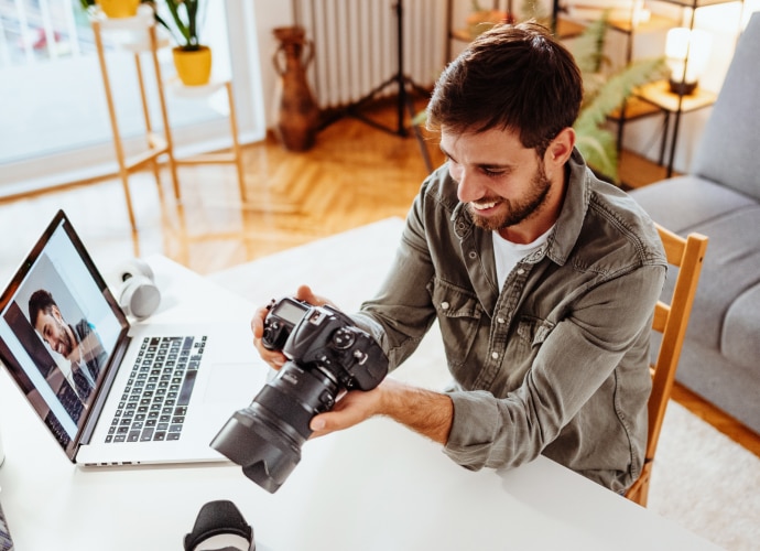 A person holding a camera with laptop on the desk.