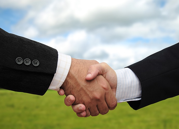 Two business men are shaking hands on the green background.