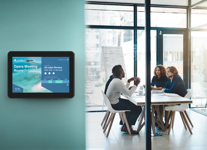 Meeting room with people talking and tablet outside indication the room booking status