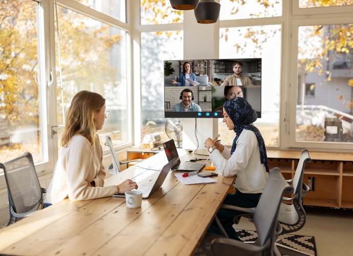 Meeting room with 2 people working at laptops and a large display showing online meeting