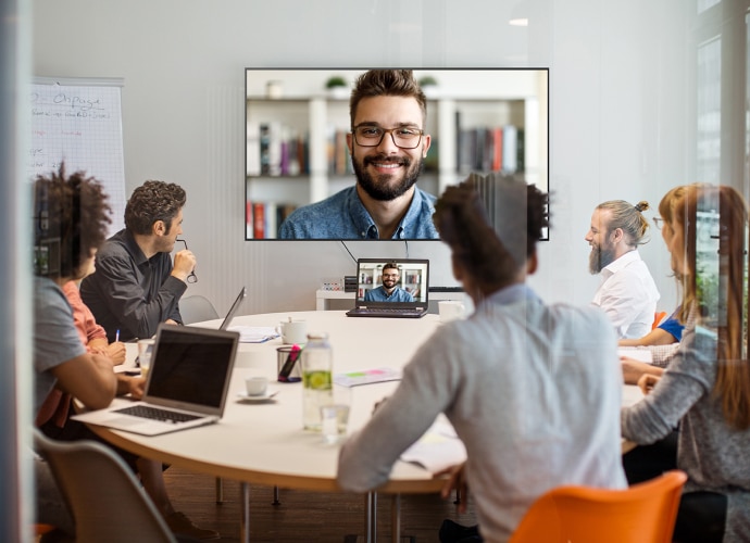 Meeting room with people around the table and a screen with presenter joining online