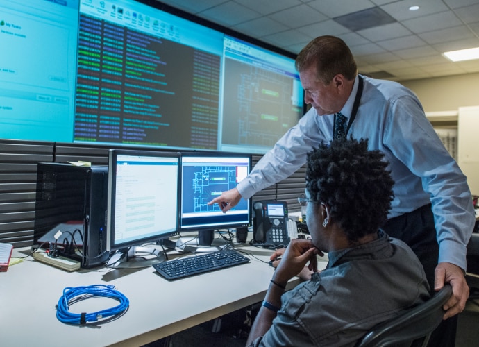 2 people discussing content of multiple screens with wall of information screens behind them