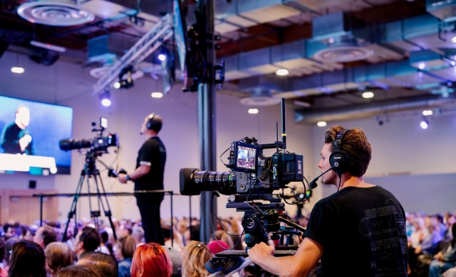 Camera operators with Sony cameras in audience for faith-based event.