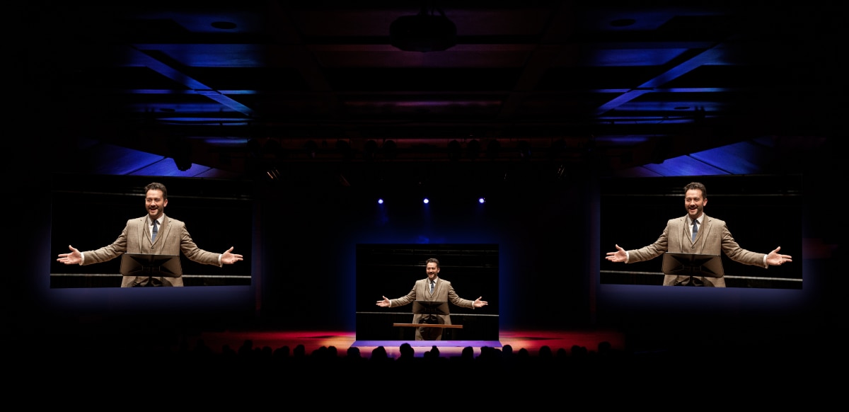 Crowded faith-based auditorium with three large screens.