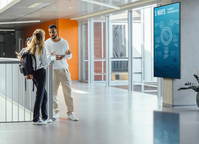 Two students talking in a university hall with a BRAVIA display on the wall