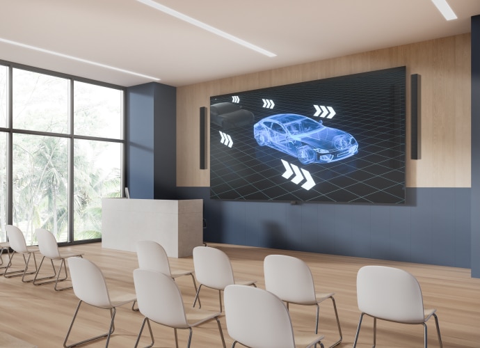 A lecture theatre with Bravia display on the wall showing 3D model of car