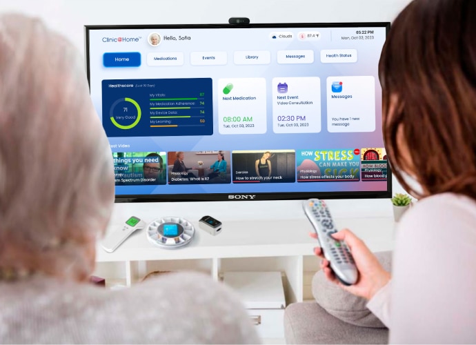 Two women face a BRAVIA display showing a digital dashboard for “Clinic@Home”, displaying different sections and metrics, as well as scheduled medication and appointment times.