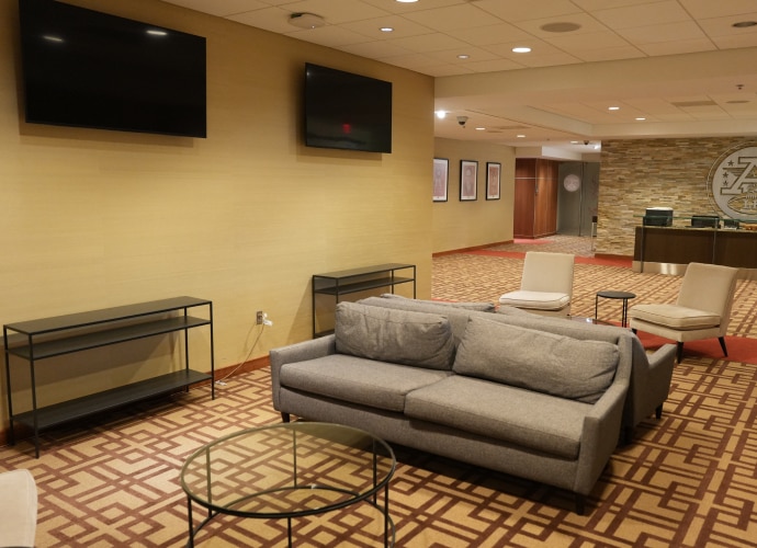 A lounge area with a gray sofa, a glass coffee table, and a few armchairs. Two BRAVIA displays mounted on the wall.