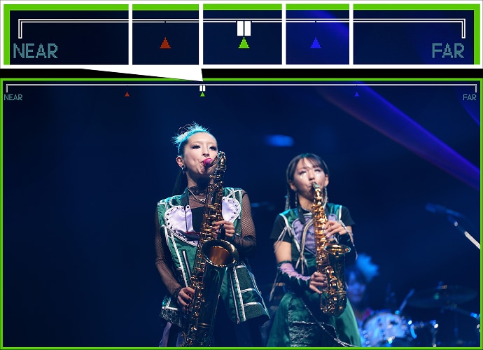 Two musician girls in green costumes are playing brass instruments live on stage. Rich focus assist functions are shown on top.